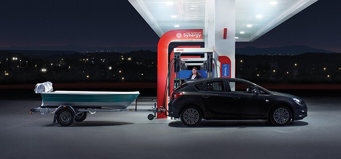 A woman with her black car and a small boat behind it uses the pump at one of the Esso stations.
