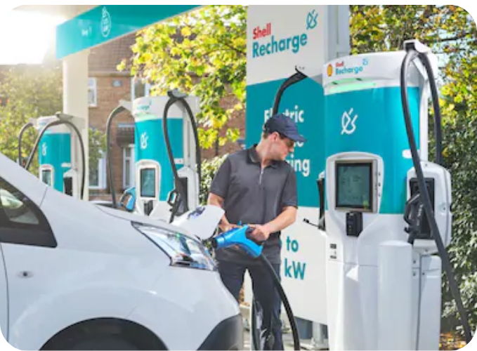Driver charging an electric vehicle at a Shell Recharge ultra-rapid EV charging station in the UK using public electric vehicle charging infrastructure.
