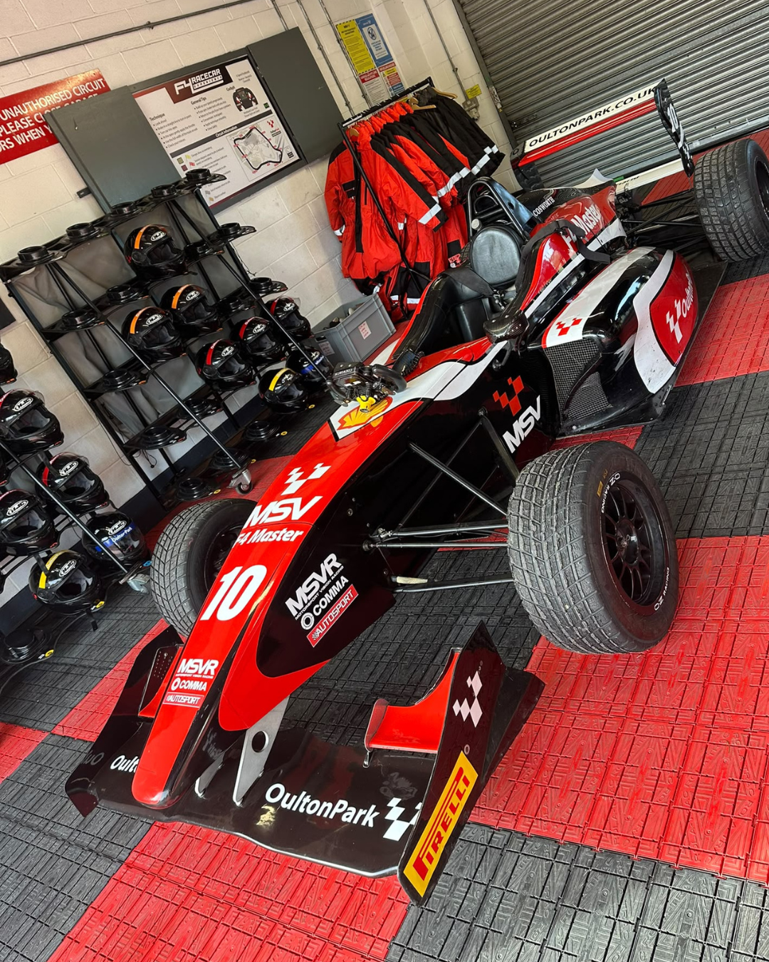 Red Formula 4 single seater in the Oulton Park garage, with racing helmets and suits ready for the track day.