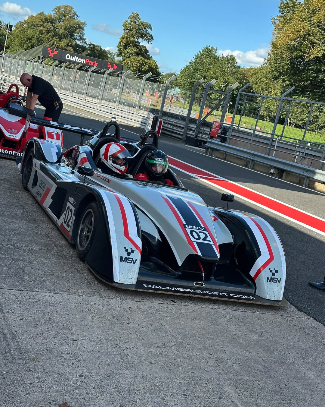 Two helmeted occupants in a JPLM sports prototype in the Oulton Park pit lane.